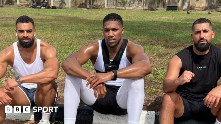 Anthony Joshua: Tributes as two team members die in fatal crash in Nigeria Anthony Joshua sits between Sina Ghami and Latif Ayodele as all wear training kit, with a grassy area behind the three men