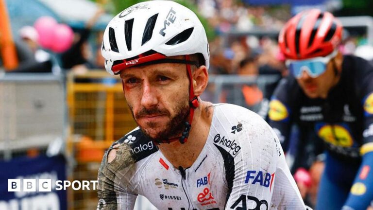 Adam Yates: Injured British cyclist out of Giro d’Italia after 30-rider crash Adam Yates in a torn cycling kit and helmet, both predominantly white